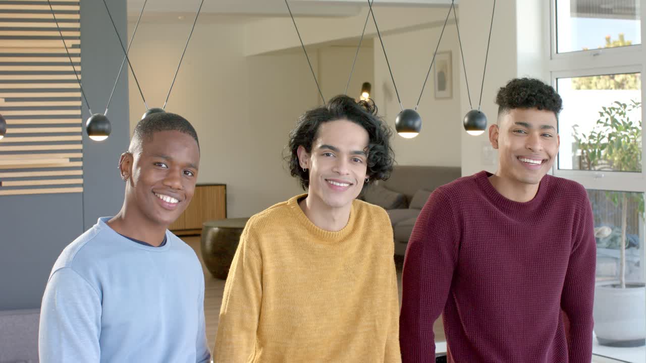 Diverse male friends facing camera leaning, smiling and nodding under pendant lights in living room