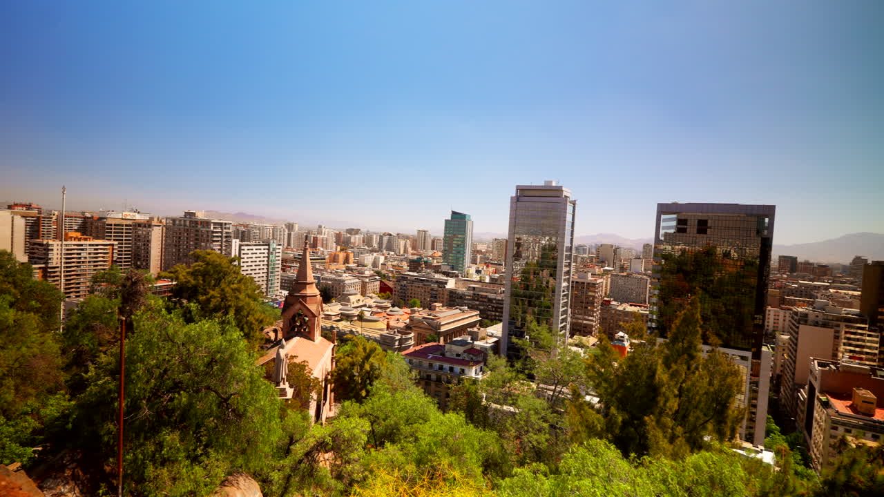 Modern glass skyscrapers reflect Santiago’s skyline on a clear day, viewed from Cerro Santa Lucía park, capturing urban growth against a distant mountainous backdrop