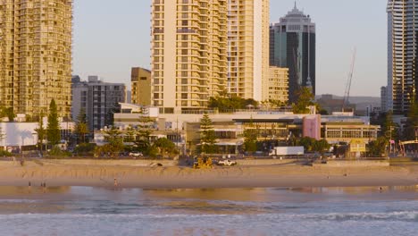 drone footage captures gold coast's beachfront skyline with high-rise buildings and sandy shores during sunset, creating a warm, serene atmosphere