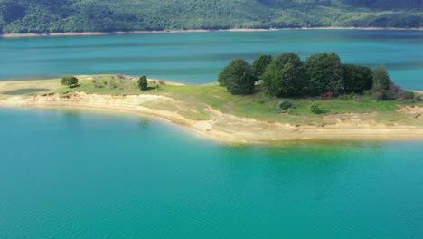 small island with tree group in rama lake bosnia and herzegovina, aerial flyover shot