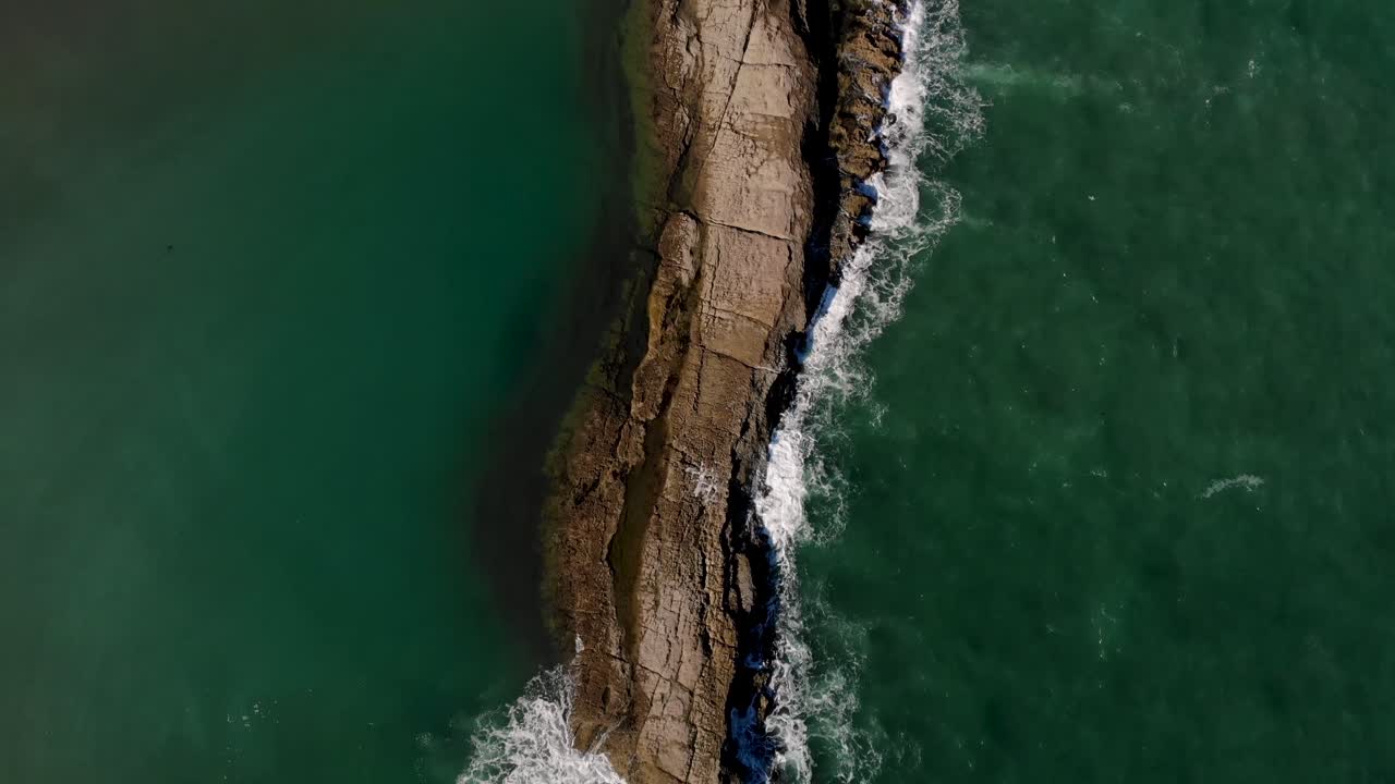 las olas del océano chocan contra el arrecife de piedra caliza, la inclinación aérea revela el faro escénico y el horizonte