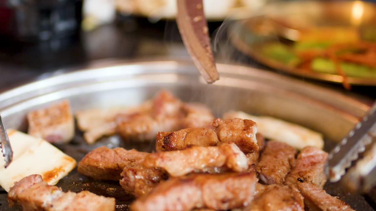 Juicy pork belly lifted from sizzling grill with metal tongs, warm lighting, shallow focus