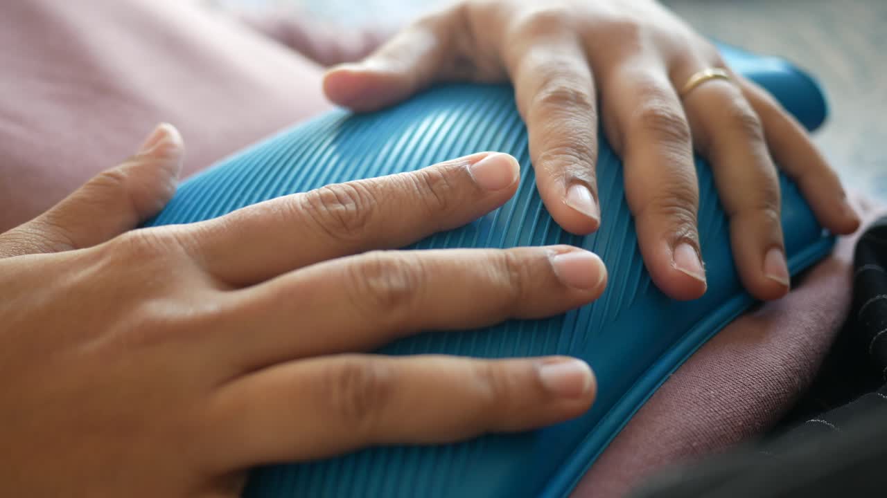 통증 완화 를 위해 뜨거운 물 병 을 들고 있는 여자