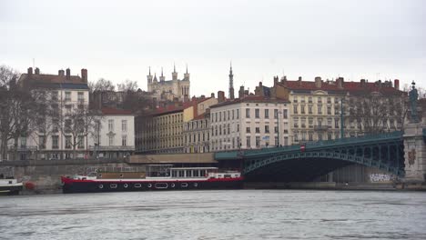 Barcos-Anclados-A-Lo-Largo-De-Las-Orillas-Del-Río-Ródano-En-Lyon,-Cerca-Del-Antiguo-Puente-De-Hierro:-Escena-Tranquila-Junto-Al-Mar