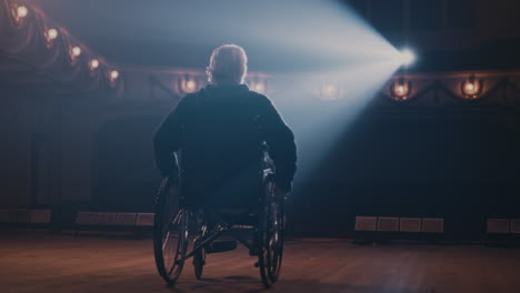 unrecognizable senior actor on wheelchair back view on anonymous aged man on wheelchair riding on stage in spotlight during performance in theater