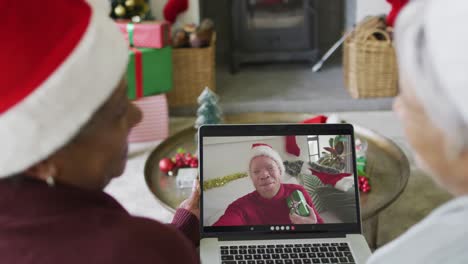 diversas amigas mayores usando una computadora portátil para una videollamada de navidad con un hombre sonriente en la pantalla
