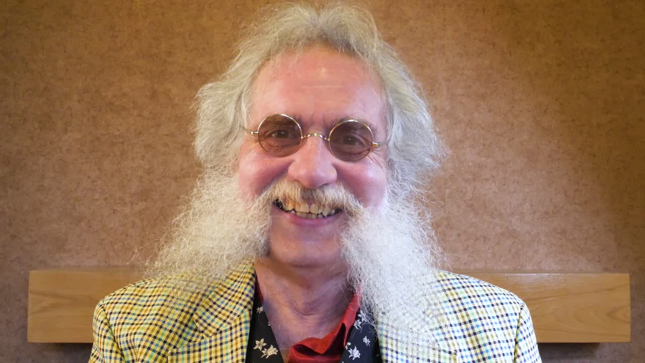 un hombre mayor con barba se pone gafas y nodos ante la cámara con una gran sonrisa