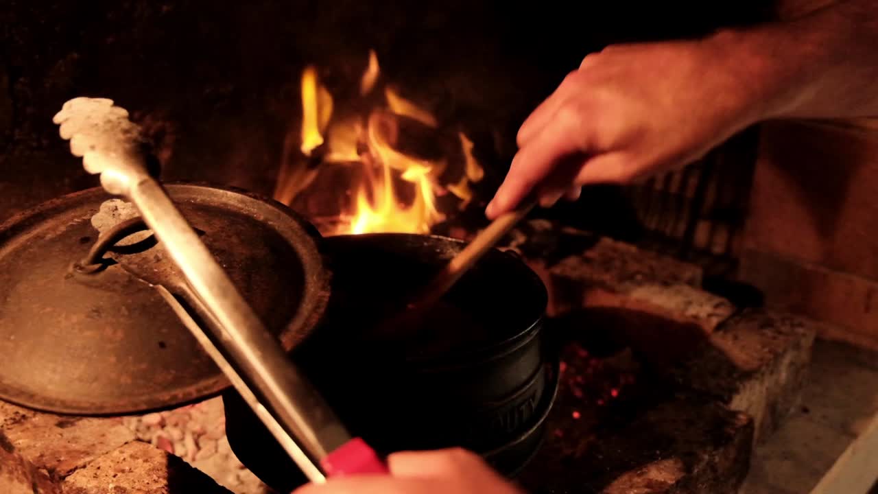 agitando una olla de potjie con una cuchara de madera cocinando en un fuego abierto