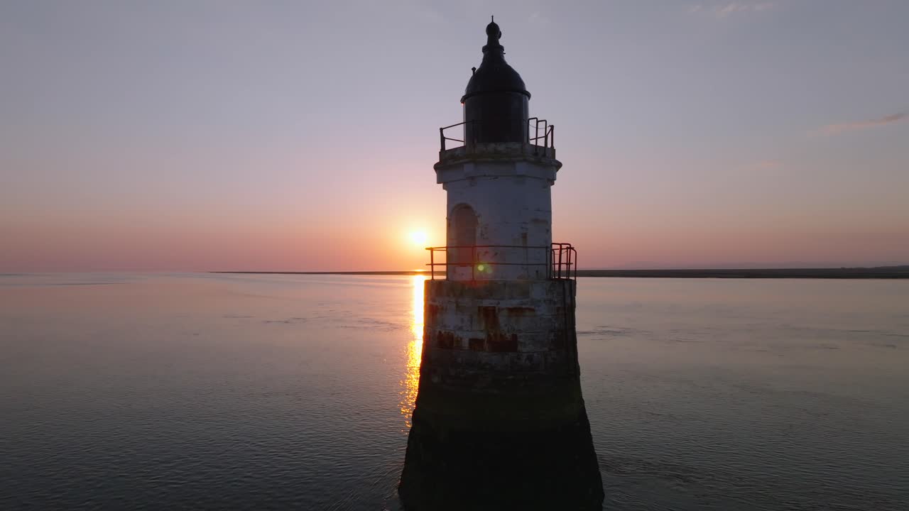 Abandoned derelict lighthouse in very calm waters with setting sun appearing from behind structure. Plover Scar Lighthouse, Lancashire, UK.
