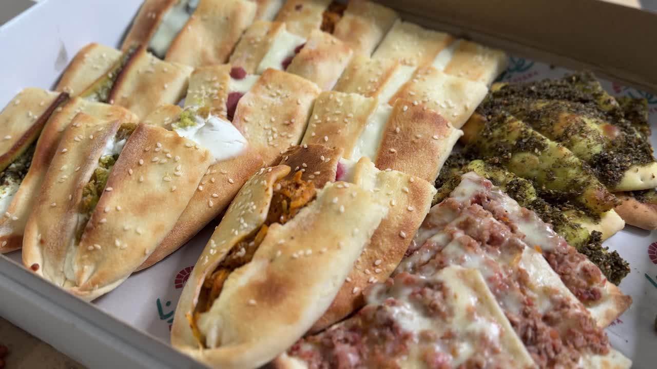 Close-up of assorted Middle Eastern flatbreads with sesame seeds, cheese, meat, and herbs in a takeaway box, perfect for food delivery, restaurant, culinary, cultural cuisine, lifestyle