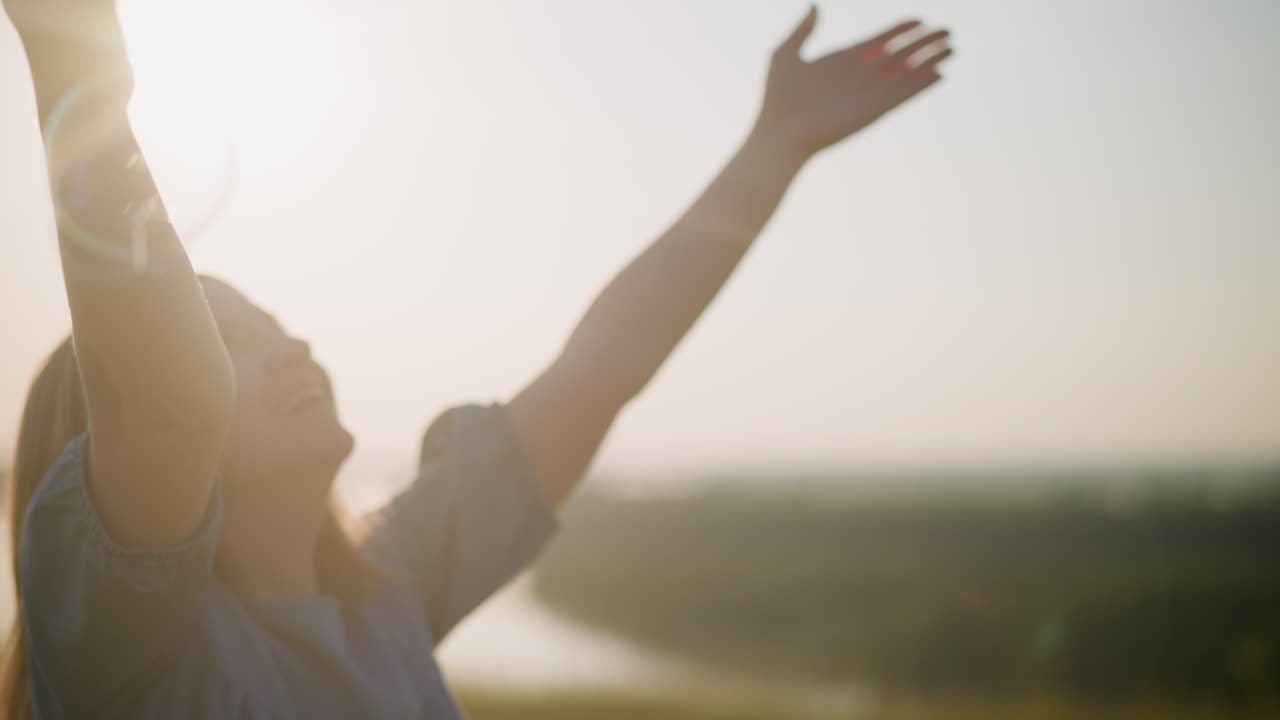 A close-up shot of a woman in a blue dress with her hands raised joyfully as she jumps under the bright sun, capturing the warmth and happiness of the moment with beautiful sun flares