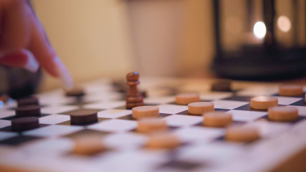 Primo piano di una mano che muove pezzi degli scacchi su una scacchiera, concentrandosi principalmente sul movimento e sull'interazione con i componenti del gioco in legno. La scena presenta quadrati alternati bianchi e neri.