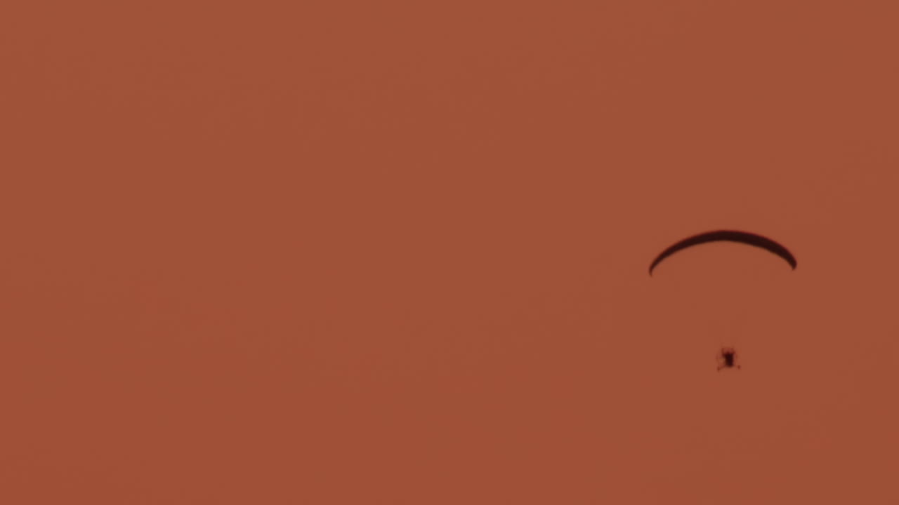 A paramotor glides smoothly through a warm toned sky at sunset