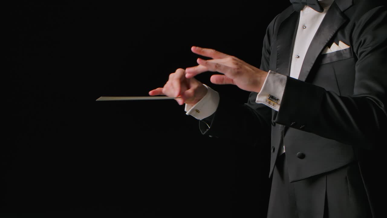 심포니 오케스트라의 지휘자는 옷을 입고 검은 바탕에 고립된 막대기의 움직임으로 음악가들을 지휘하고 있으며, 가시적인 몸짓으로 음악 공연을 지휘하고 지휘하고 있다.