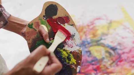 video of biracial female artist hands, painting palette and brush