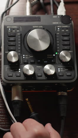 una toma de primer plano de una mano conectando un cable a un mezclador de sonido, con el dispositivo encendido. el detalle técnico y la precisión involucrados en la configuración de equipos de audio, con varios botones, diales