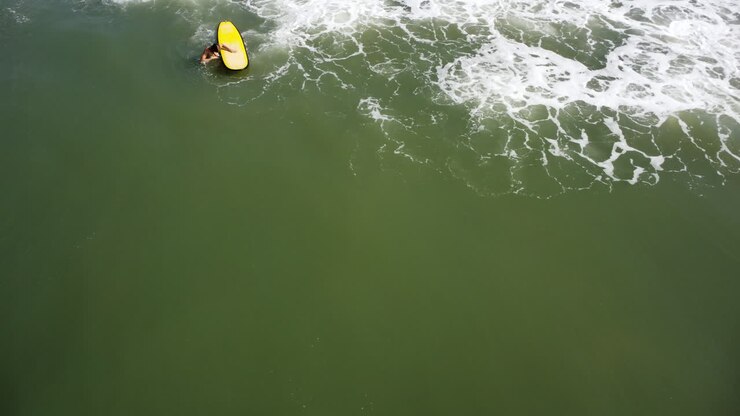 Static aerial birdseye shot of woman with yellow surfboard riding against wave