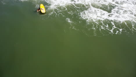 vista aérea estática de una mujer con una tabla de surf amarilla cabalgando contra una ola