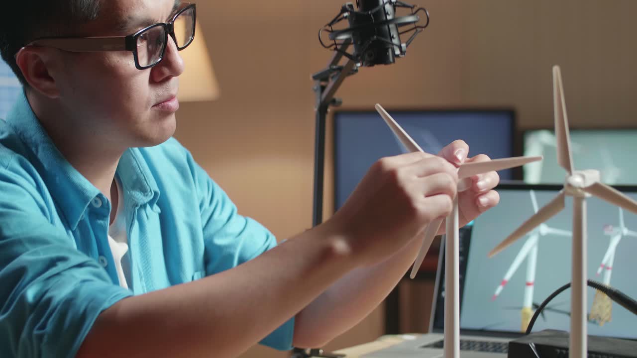 Primo piano di un uomo asiatico scontento per il fallimento nel testare la turbina eolica mentre lavora con un laptop accanto al pannello solare in ufficio