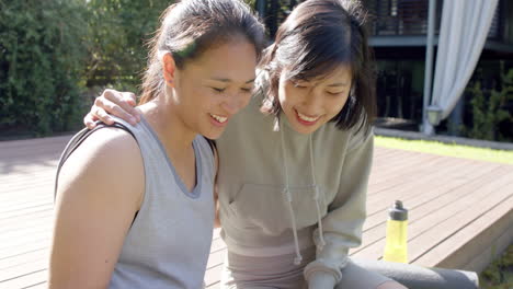 Happy-asian-female-friends-with-water-bottle-doing-selfie-and-smiling-on-terrace,-slow-motion