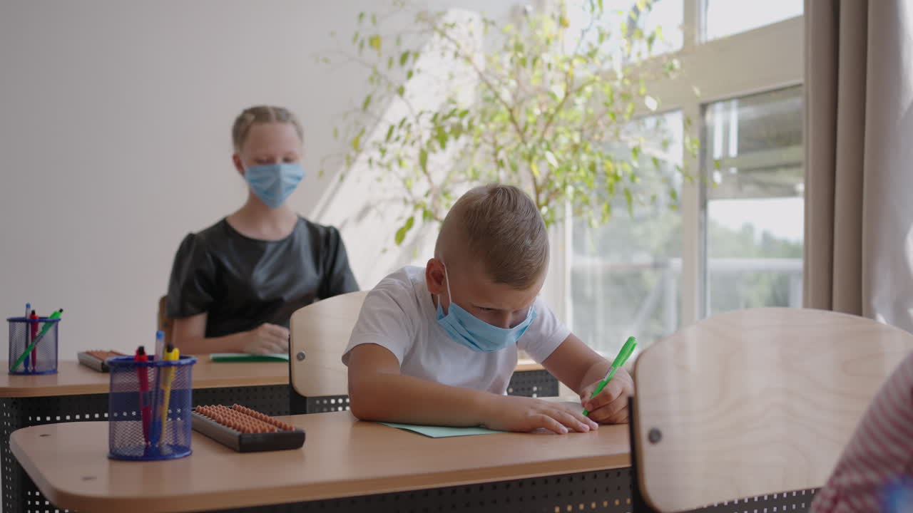 학교에서 교실에서 아이들은 사회적 거리를 지키며 보호 마스크를 착용하여 노트북에 글을 쓴다. 전염병 동안 학교 교육