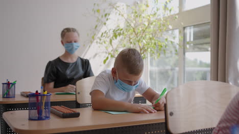 At-school-in-the-classroom-children-write-in-notebooks-in-protective-masks-observing-a-social-distance.-School-education-during-the-pandemic