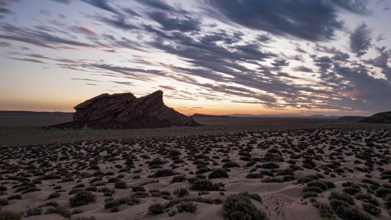 Wide-angle shot of a desert landscape at sunset, capturing dramatic clouds and a rocky formation
