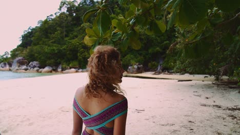 A-young-brunette-woman-is-enjoying-the-view-upon-a-tropical-beach,-the-turquoise-sea-water-and-green-lush-mangrove-trees-on-the-Perhentian-Islands-in-Malaysia-in-slow-motion