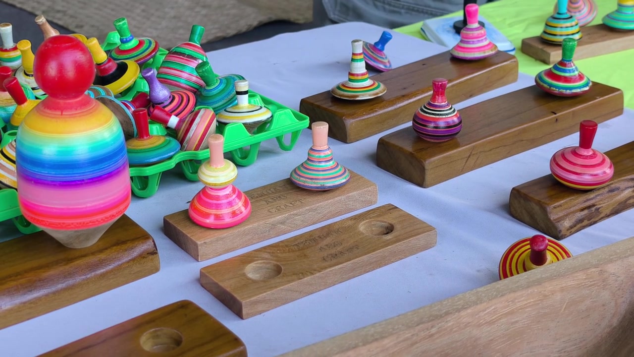 Colorful gasing sepetik tops are displayed on a table for sale. Vibrant paint is carefully applied in concentric rings on their wooden surfaces. This showcase captures authentic regional heritage craf