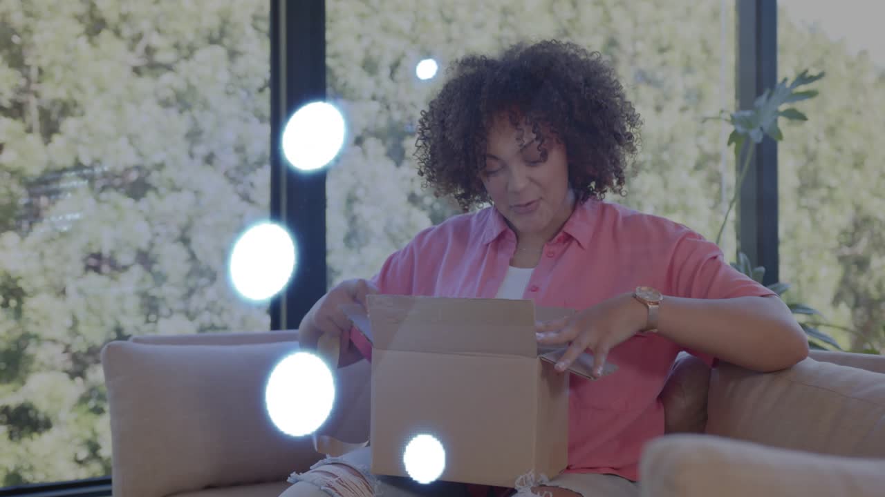 Woman sitting on sofa shifting box, peeling tape, opening box and inspecting ecommerce purchase