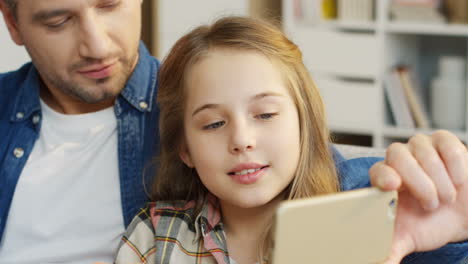 close up of the nice family sitting on the couch and hugging while the father showing something on the smartphone