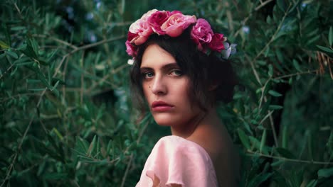 cinemagraph - seamless video loop of a young caucasian female model - woman with a flower wreath and the wind moving her pink dress and hair and the green olive trees in the back