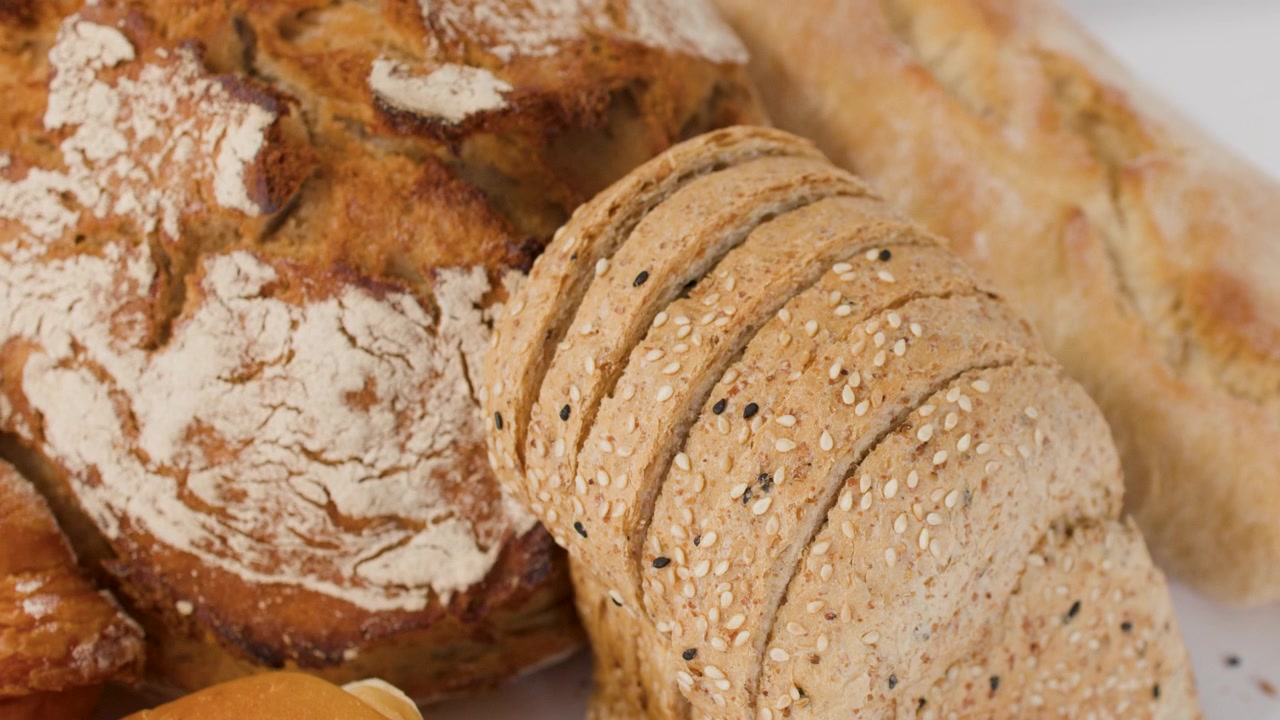 Close-up slow camera pan across various crusty loaves, sliced bread, and golden croissants.
