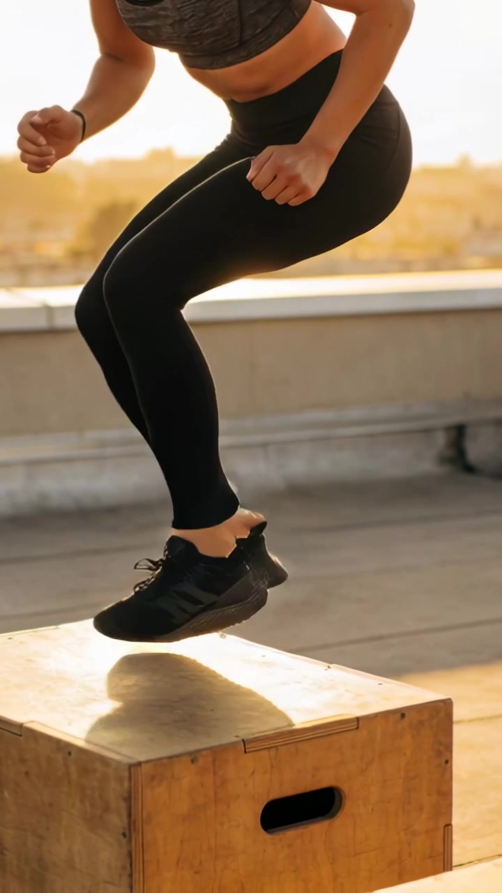 Video verticale: Inizio squat, donna che fa salti sulla scatola sul tetto usando la pliometria per la potenza, in reggiseno sportivo