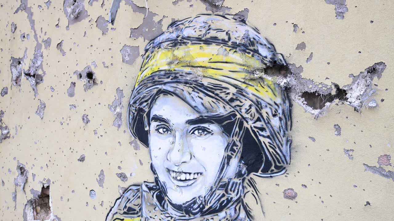 A close-up view of a mural of a Ukrainian soldier, framed by real bullet and shrapnel holes, on a heavily damaged building in Irpin, Ukraine, during the Ukraine-Russia conflict.
