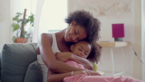 happy black woman and cute little girl sitting on couch and hugging at home