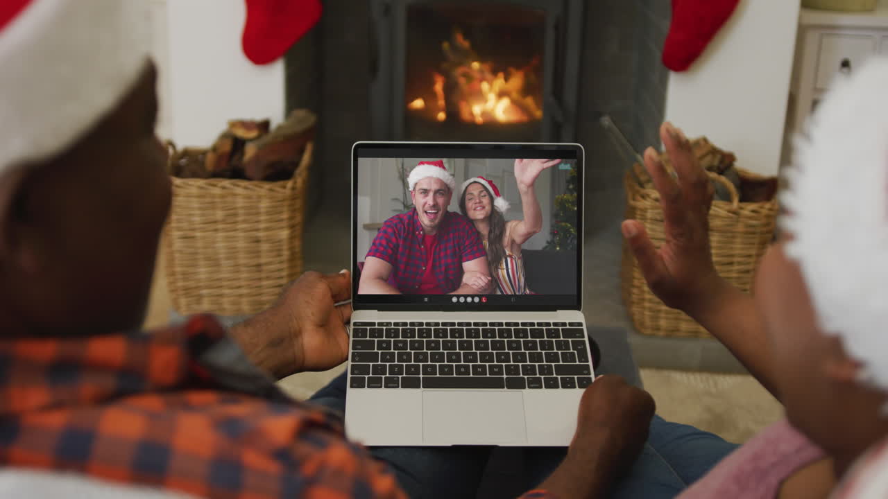 pareja afroamericana usando una computadora portátil para una videollamada de navidad con amigos sonrientes en la pantalla