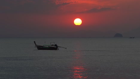 a long tail boat sits on the sea in front of a beautiful sunset