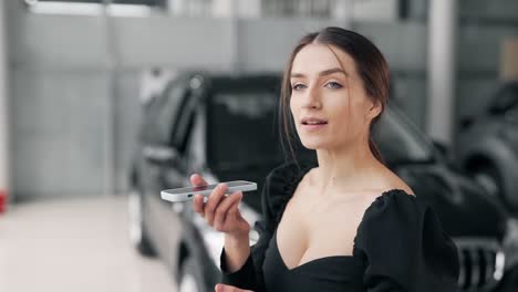 sexy girl writes a voice message on a smartphone on the background of the car show