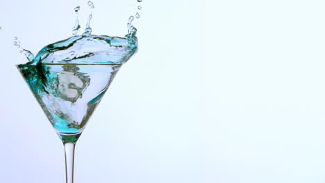 ice falling into cocktail glass of blue alcohol on white background