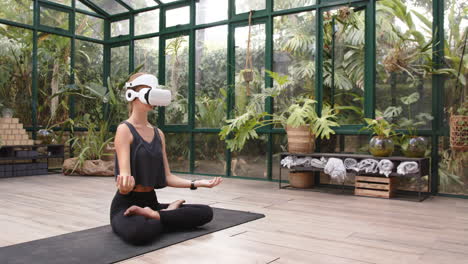meditating on yoga mat, woman using vr headset in glass house studio, copy space