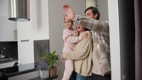 A-happy-brunette-girl-in-a-beige-sweater-carries-her-daughter-in-pink-clothes-in-her-arms-and-together-with-her-boyfriend-enters-a-modern-apartment-after-moving.-A-happy-family-enters-a-new-apartment-after-moving-in