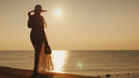 A-Romantic-Woman-With-Shoes-In-Her-Hand-Is-Standing-On-The-Pier-Meets-The-Dawn-Dreams-And-Trips-Conc