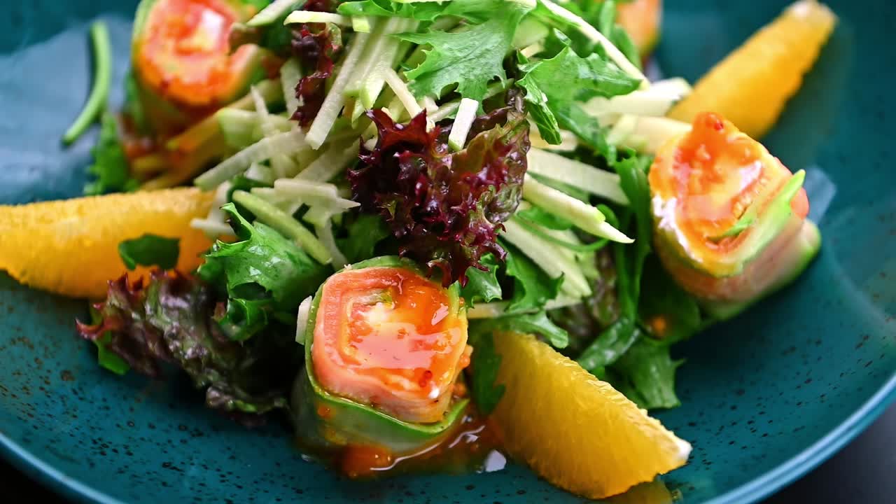 Friske forårsruller med salat og frugt serveret i en blå skål på en restaurant. Forårsruller med krydderurter og salat ligger på en blå tallerken med appelsinskiver