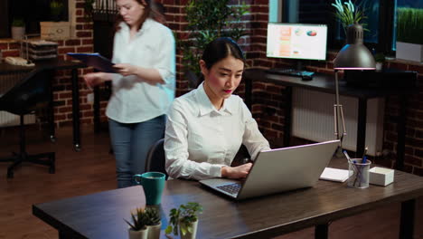 Smiling-woman-sitting-down-at-office-desk,-typing-on-laptop-keyboard