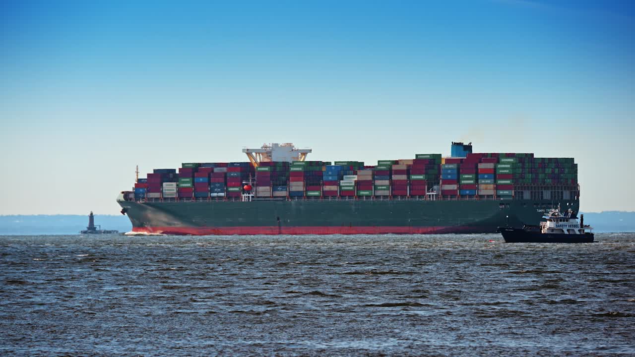 New York, USA, 5 October 2025: Side view of a green container ship at sea. Profile of a large freighter with colorful containers on deck and a small boat nearby