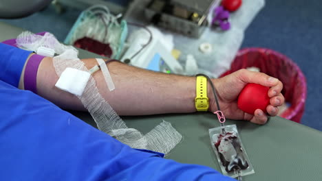male hand with a yellow wrist watch holding a red rubber heart. blood is taken from a donor. close up.