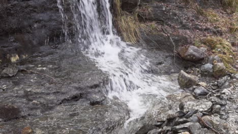 Agua-Cayendo-De-Una-Cascada-Mediana-Con-Rocas-De-Color-Marrón-Oscuro