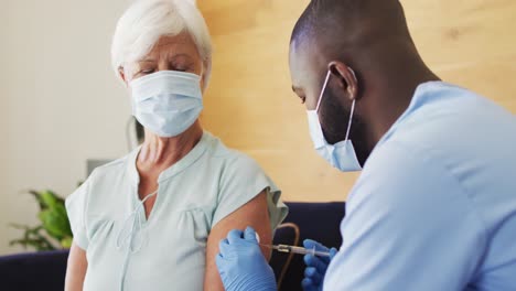 video of african american male doctor in face mask vaccinating caucasian senior woman