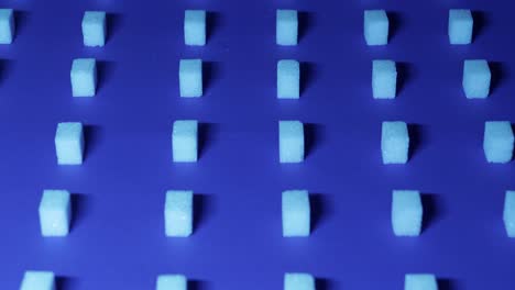 una vista muy lenta inclinada hacia abajo de un fondo cúbico único con cubos de azúcar blanco dispuestos en filas sobre un fondo azul oscuro, efecto 3d